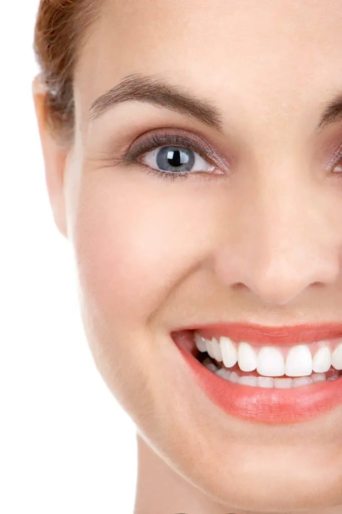 Close-up of a woman's face with a bright smile, showing clear skin and healthy white teeth. 