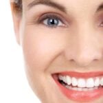 Close-up of a woman’s face with a bright smile, showing clear skin and healthy white teeth.