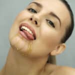 Close-up of a smiling woman with honey dripping down her chin, licking her lips playfully.