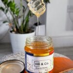 A jar of HoneyBee & Co. Acacia Honey with a honey dipper, showcasing its golden colour and smooth texture. Pure raw British and European honey available from your local honey shop in the UK.