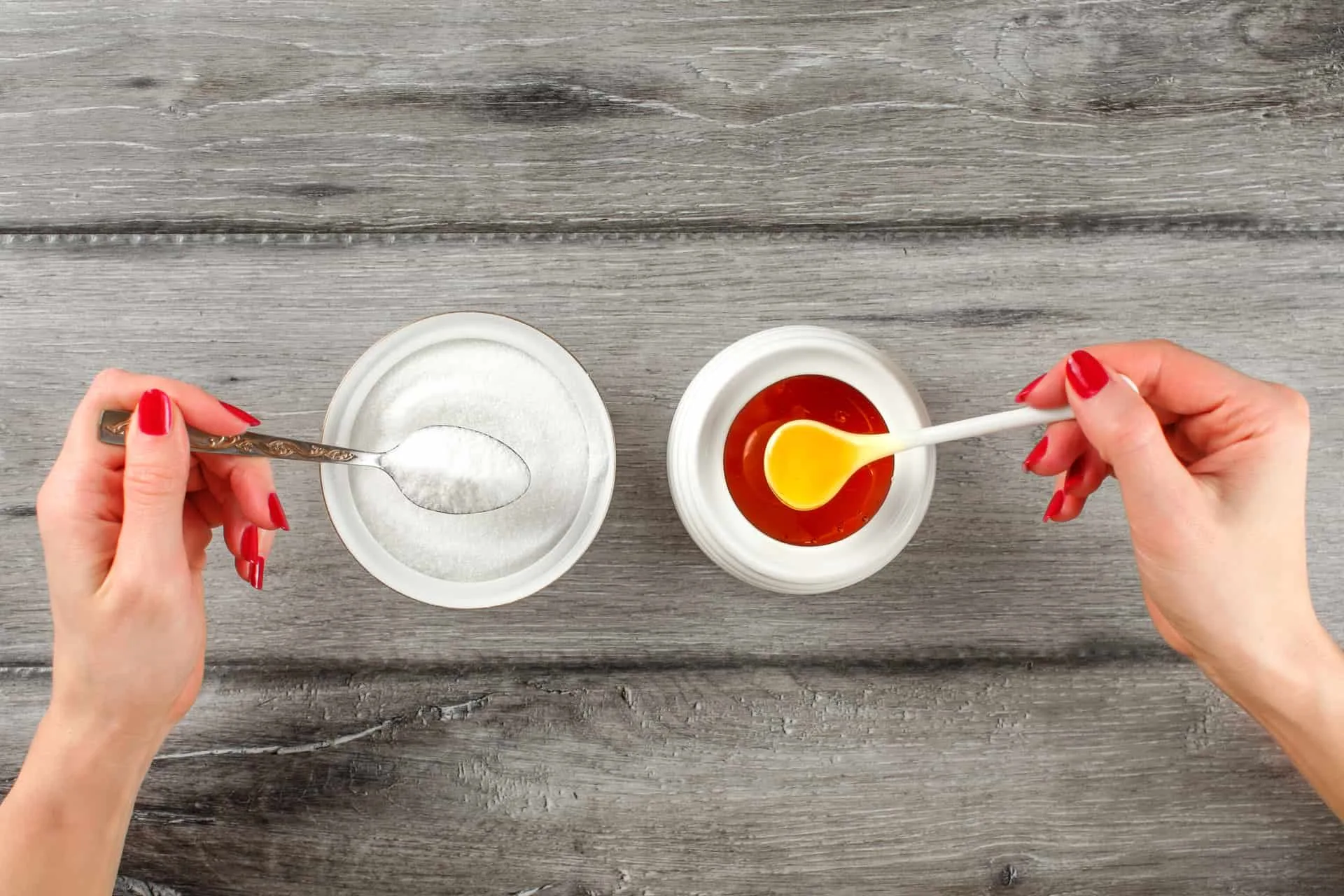 Top view on young woman hands with red nails, holding spoon full of sugar and honey in other hand. Sugar vs honey concept. Top view on young woman hands with red nails, holding spoon full of sugar and honey in other hand. Sugar vs honey concept.