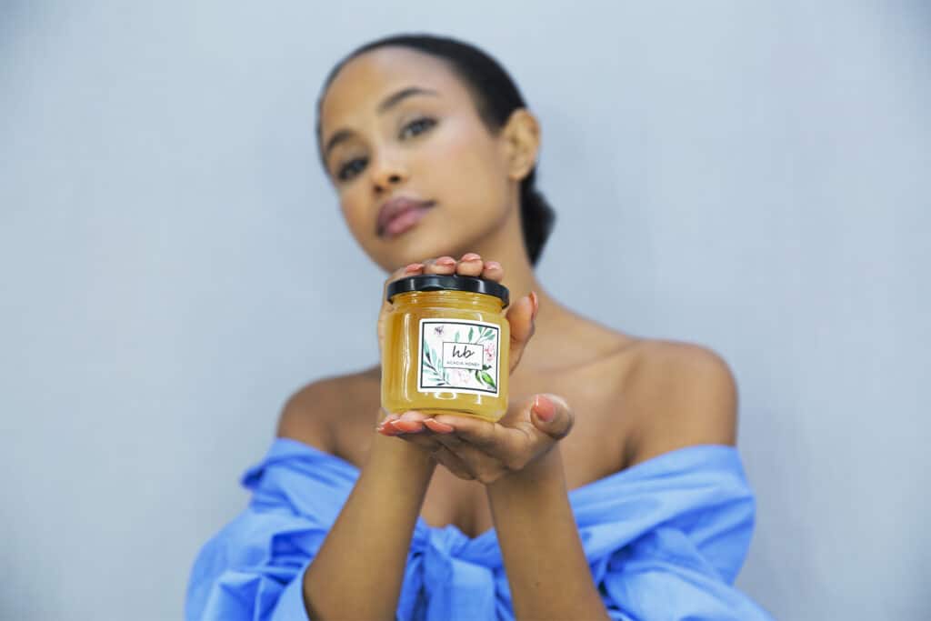 Model holding a jar of raw honey from HoneyBee & Co., showcasing the brand’s natural honey in a minimalist lifestyle setting.
