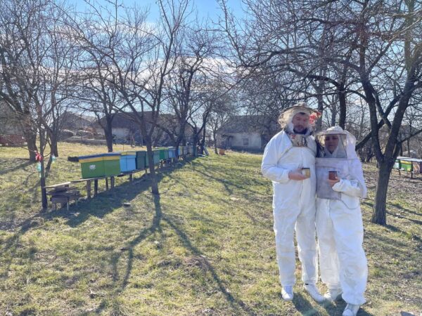 Acacia Honey. Beekeepers in protective suits standing beside colourful hives in a Romanian countryside apiary, representing HoneyBee & Co.’s sustainable beekeeping and authentic honey sourcing.