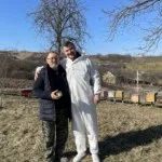 Our Founders. Nistor Fanel and Nistor Dragos. Two Romanian beekeepers standing together near colourful hives in the countryside, representing HoneyBee & Co.’s partnership with local beekeepers and sustainable honey sourcing.