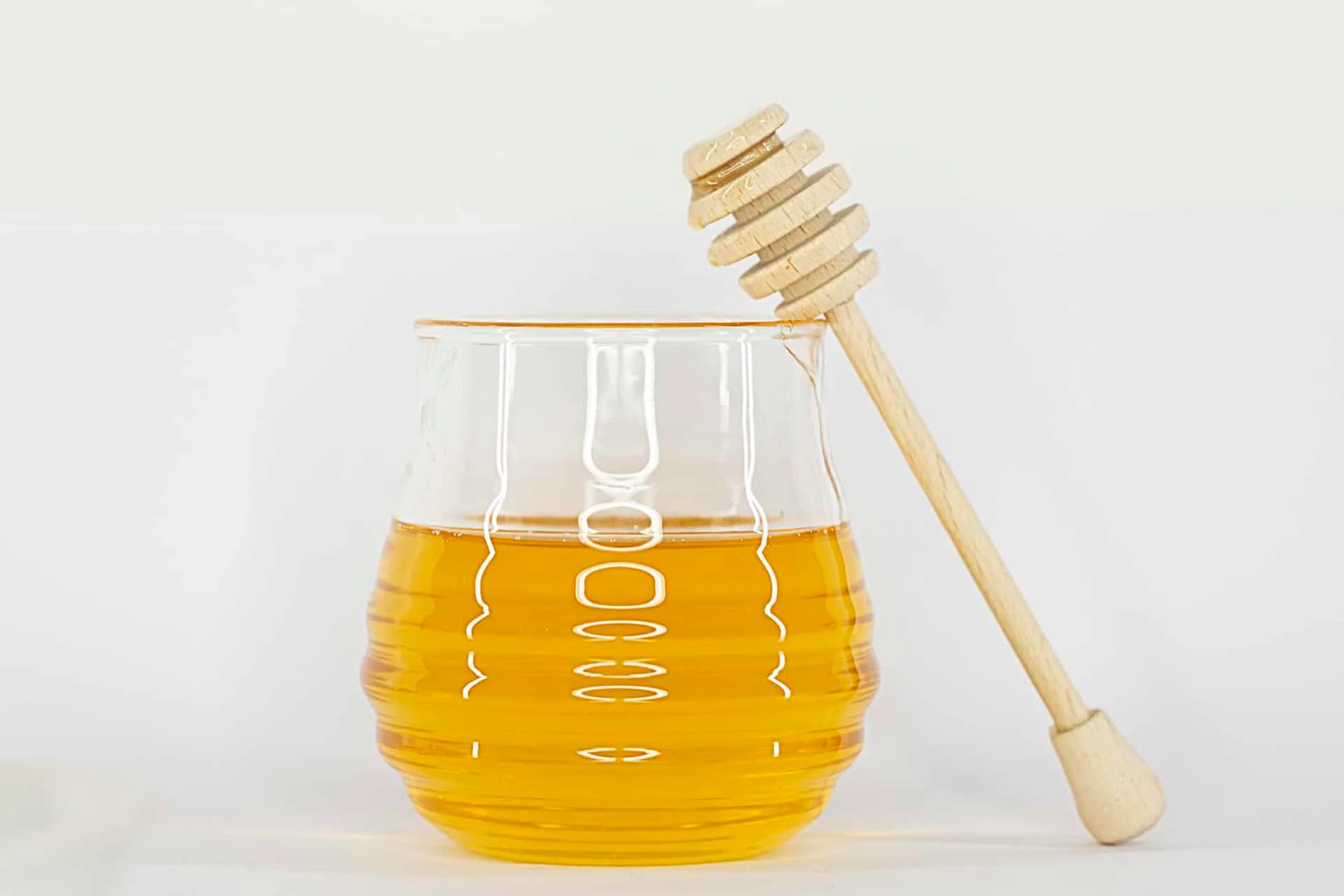 Glass of golden honey with a wooden honey dipper