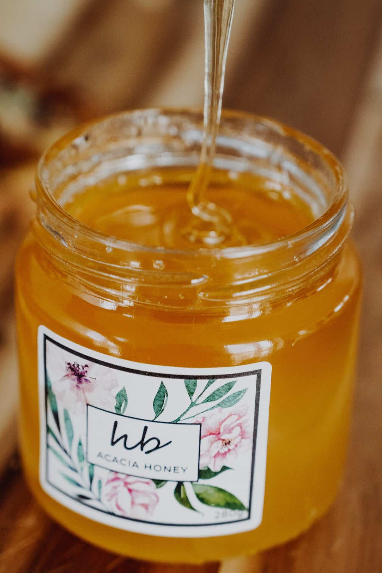 Pale golden raw acacia honey drizzling from a wooden honey dipper