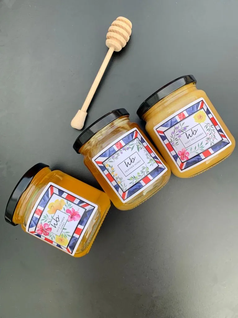 Three jars of HoneyBee & Co. British honey with a wooden honey dipper
