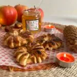 A jar of HoneyBee & Co. Acacia honey placed on a festive table with apple pastries, tealight candles, apples, and pinecones.