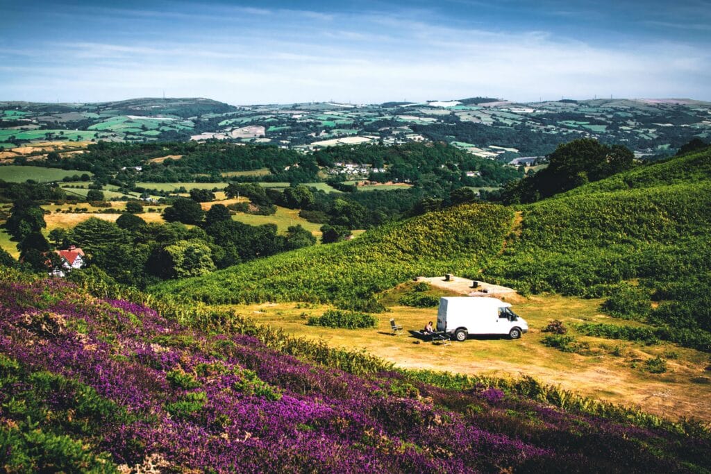 White camper van parked on a hilltop near blooming heather with panoramic views of the British countryside