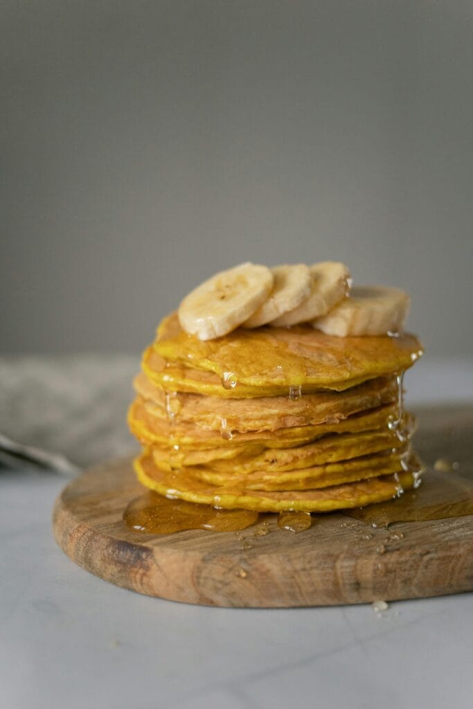 Stack of banana pancakes drizzled with golden honey on a wooden board