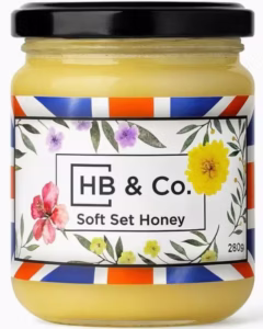 Vasetto di miele HoneyBee & Co. Soft Set da 280 g, dalla consistenza cremosa e dorata, con etichetta floreale Union Jack.
