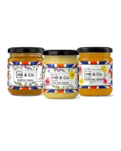 HoneyBee & Co. tre vasetti di miele con etichette floreali e coperchi neri.