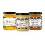 Vasetti di miele assortiti di HoneyBee & Co. con etichette colorate e coperchi neri.